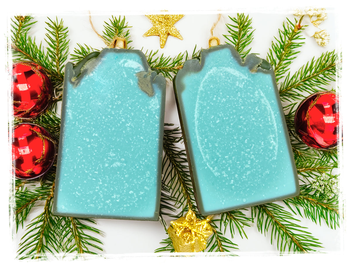 The Man goat milk soap bars in turquoise and gray, displayed with evergreen branches and holiday ornaments.
