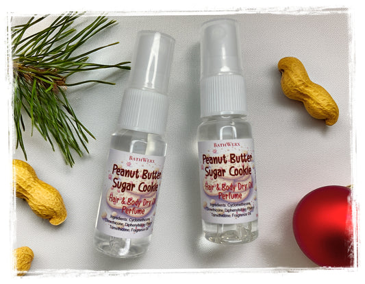 Two BathWerx Peanut Butter Sugar Cookie Hair & Body Dry Oil Perfume spray bottles styled with peanuts, pine branches, and a red ornament.