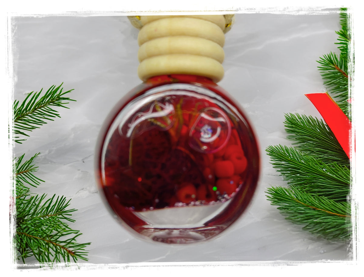 Winter Candy Apple car charm air freshener in a round glass bottle, styled with evergreen branches.