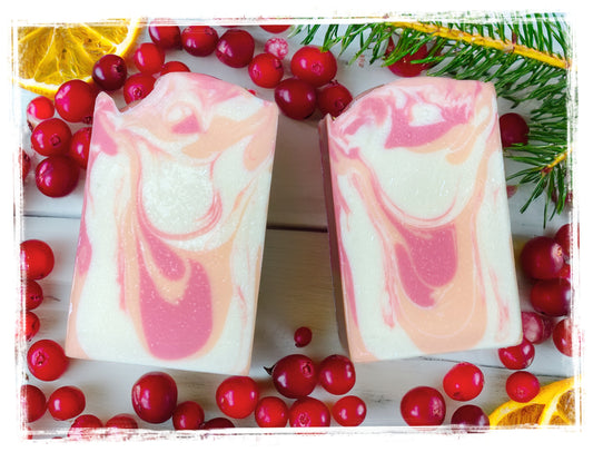 Cranberry Orange Spice soap bars with pink, peach, and cream swirls, surrounded by cranberries, orange slices, and evergreen sprigs.
