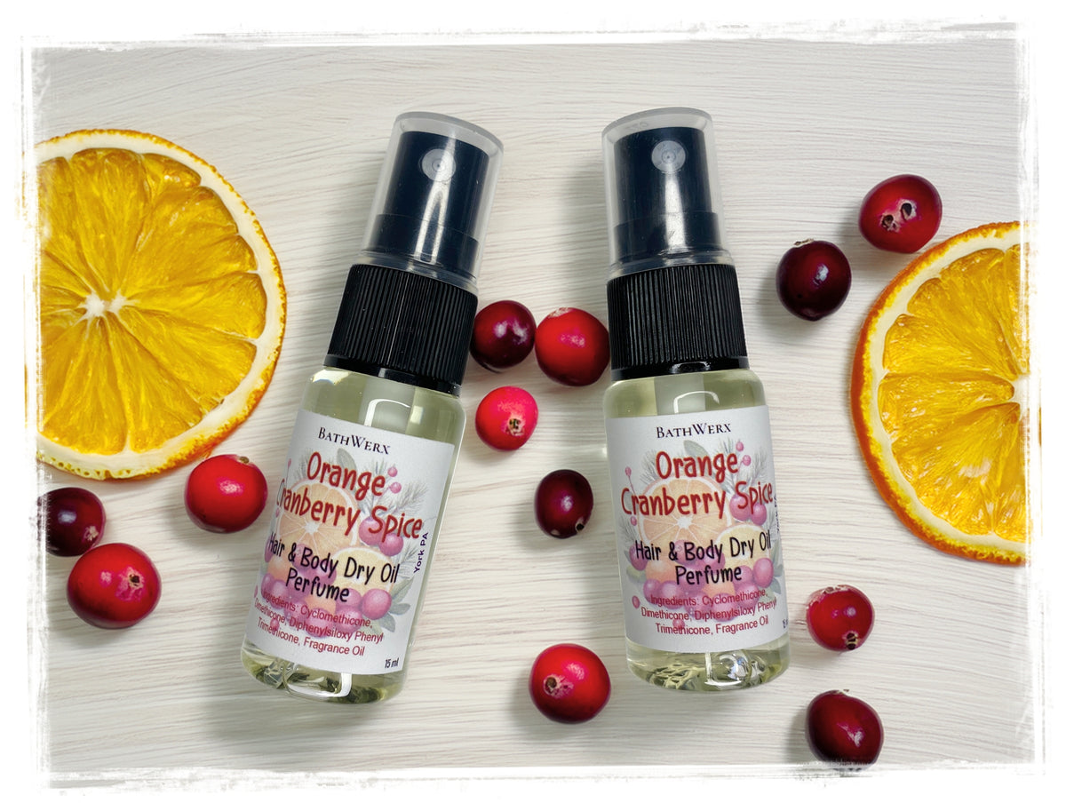Two Orange Cranberry Spice Hair & Body Dry Oil spray bottles surrounded by orange slices and cranberries.