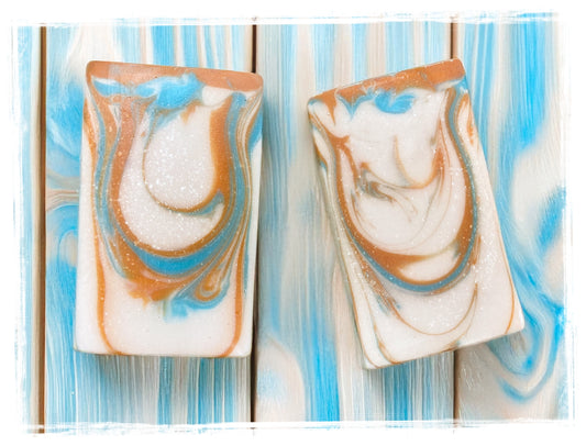 Two rectangular soap bars with marbled design on a striped background. Handcrafted Artisan Soap: Sunshine Warrior