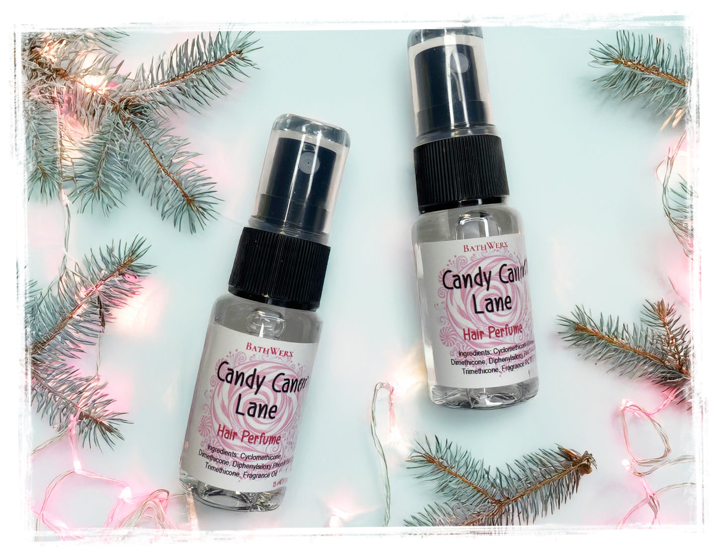 Two bottles of Candy Cane Lane hair perfume on a light blue background with Christmas tree branches.