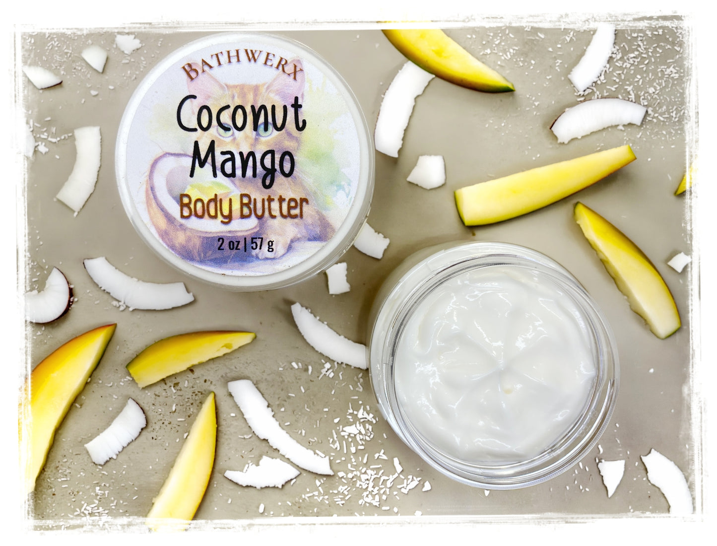 BathWerx Coconut Mango Body Butter open clear jar showing creamy white texture, surrounded by fresh mango slices and coconut pieces