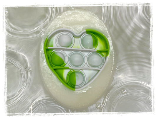 Close-up of a handcrafted kids' soap with an embedded green and white silicone pop-it fidget toy, floating on a rippling water background