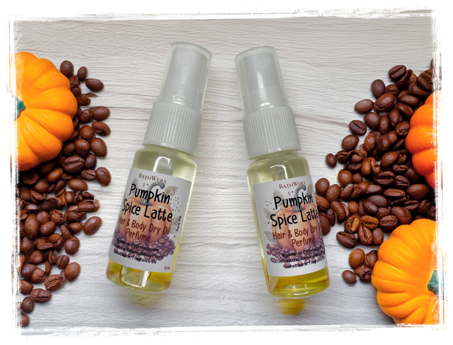 Two BathWerx Pumpkin Spice Latte Hair & Body Dry Oil Perfume spray bottles on a white wood surface, surrounded by coffee beans and orange mini pumpkins