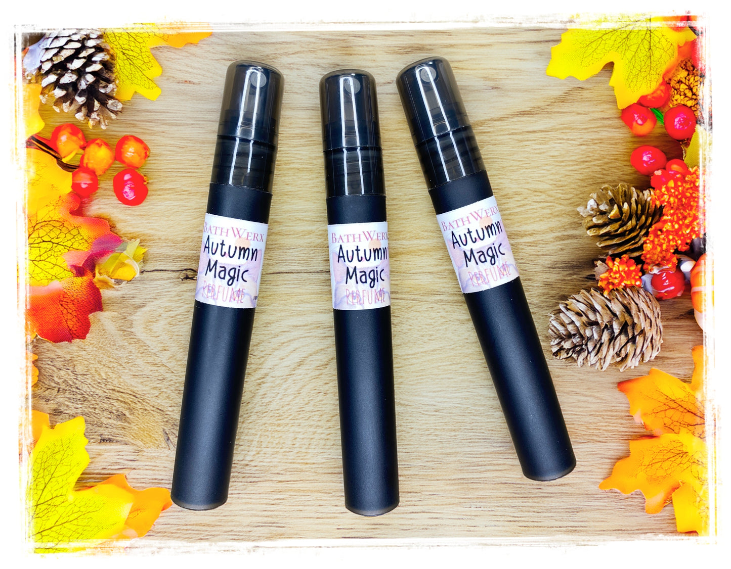 BathWerx Autumn Magic perfume sprays in matte black, styled on a rustic wood surface surrounded by colorful fall leaves, pine cones, and red berries - travel-size 10ml fragrance