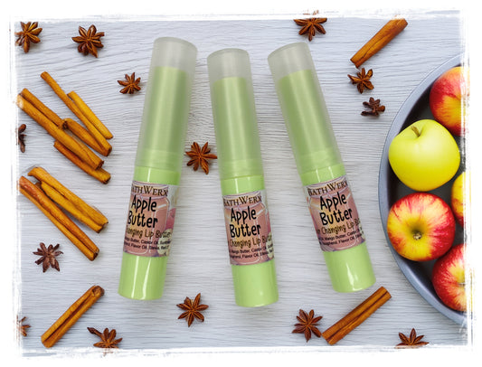Three BathWerx Apple Butter Color-Changing Lip Butter tubes in green packaging with cinnamon sticks, star anise, and fresh apples on a white wood background