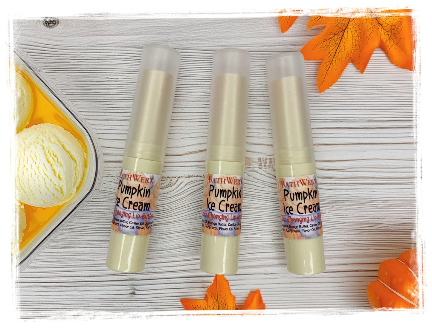 Three BathWerx Pumpkin Ice Cream Color-Changing Lip Butter tubes in cream packaging with a scoop of vanilla ice cream, fall leaves, and a pumpkin on a white wood background.