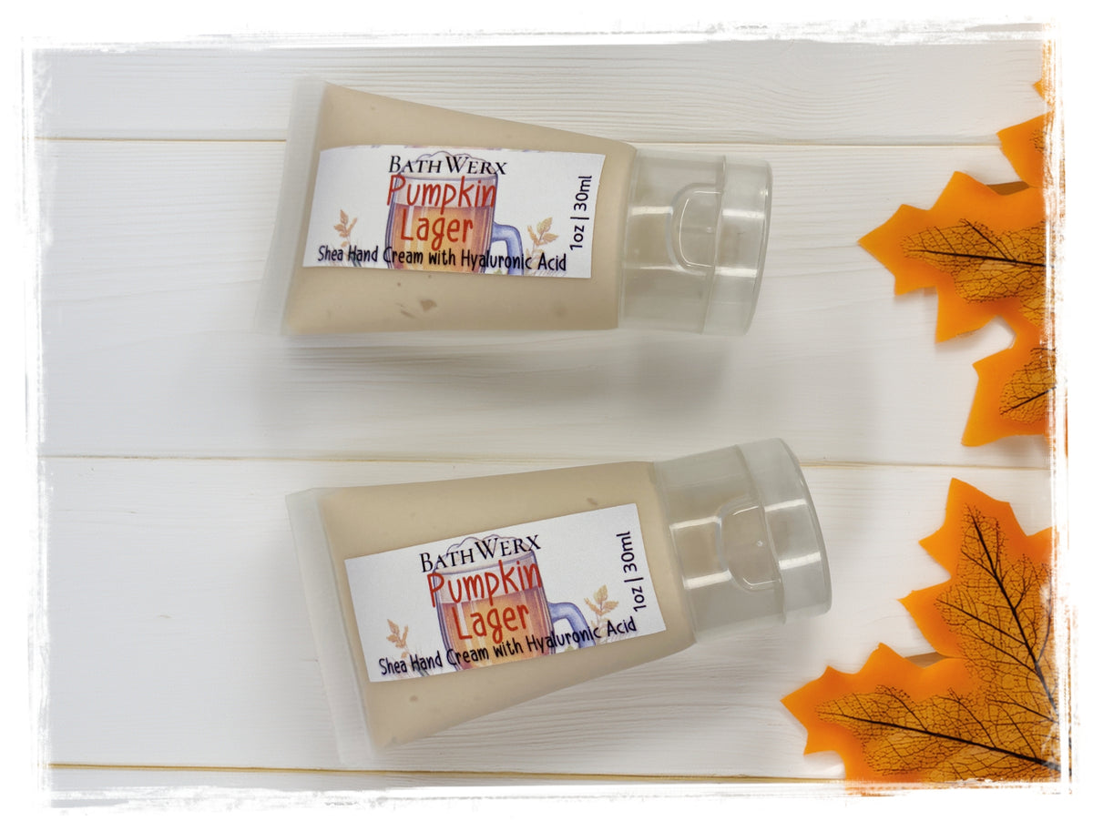 Two mini 1oz tubes of BathWerx Pumpkin Lager Shea Hand Cream with Hyaluronic Acid on a white wood background with fall maple leaves.