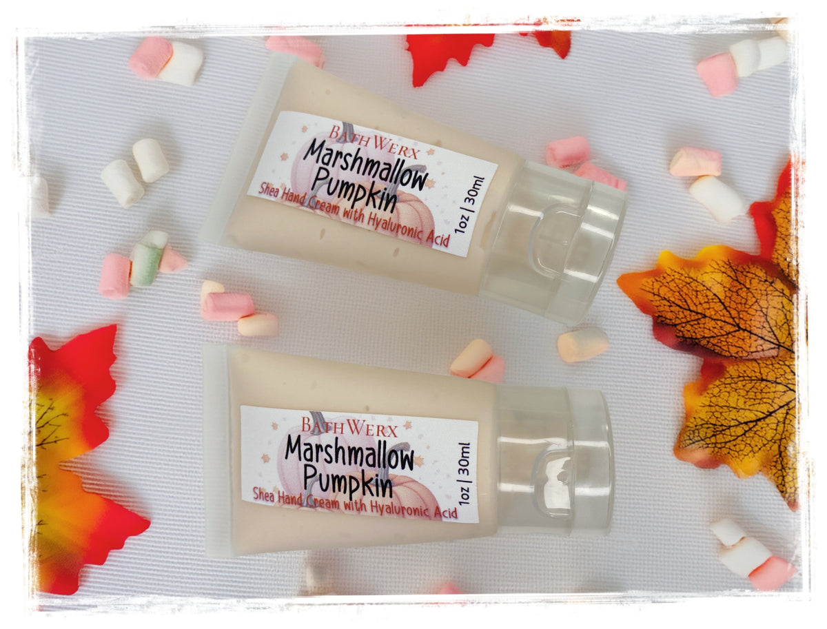 Two mini 1oz tubes of BathWerx Marshmallow Pumpkin Shea Hand Cream with Hyaluronic Acid surrounded by colorful mini marshmallows and fall leaves.