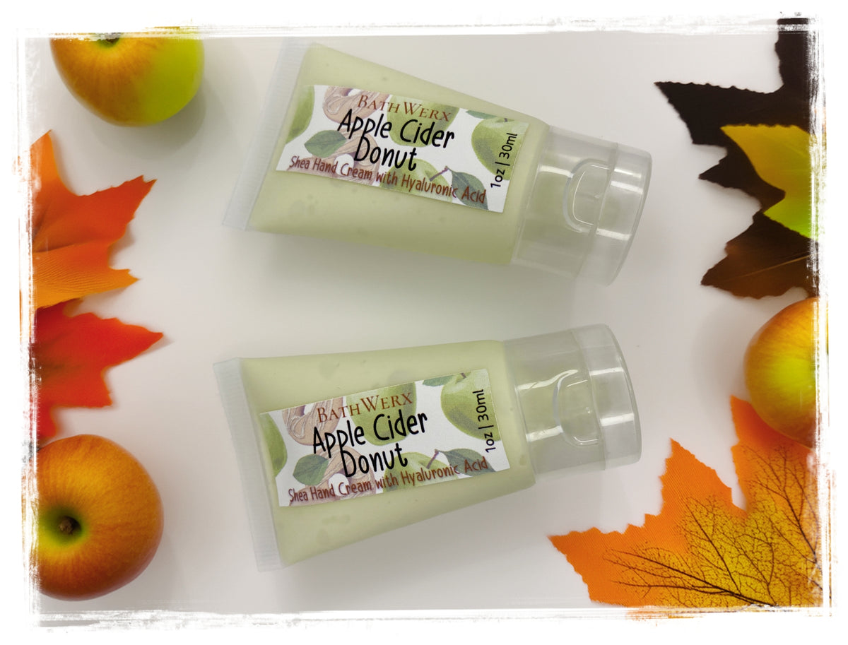 BathWerx Apple Cider Donut Shea Hand Cream with Hyaluronic Acid, 1oz travel-size pump bottles styled with fresh apples and colorful fall leaves.