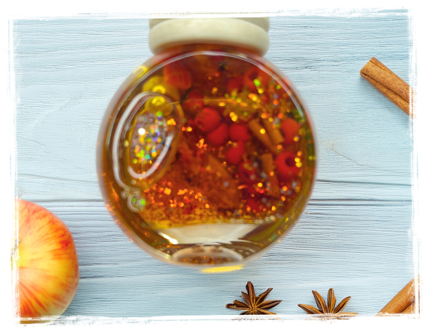 Cinnamon Apple Butter scented car charm — round glass globe with amber liquid, gold glitter, red berry embeds, and cinnamon stick accents, styled with apple, star anise, and cinnamon sticks.