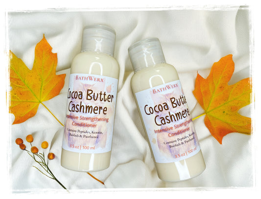 BathWerx Cocoa Butter Cashmere Intensive Strengthening Conditioner, two 3.5 oz bottles with Peptides, Keratin, Baobab and Panthenol, surrounded by fall maple leaves on a white knit background.