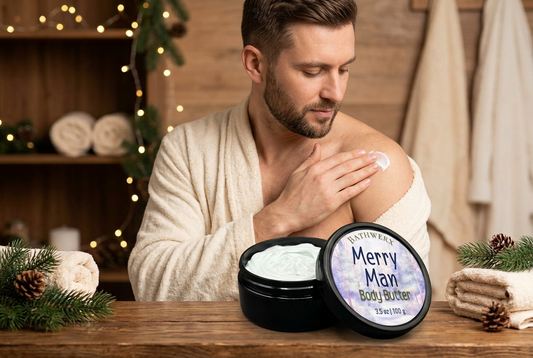 Man in a cream bathrobe applying Merry Man body butter to his shoulder, with an open jar, pine branches, and holiday lights.