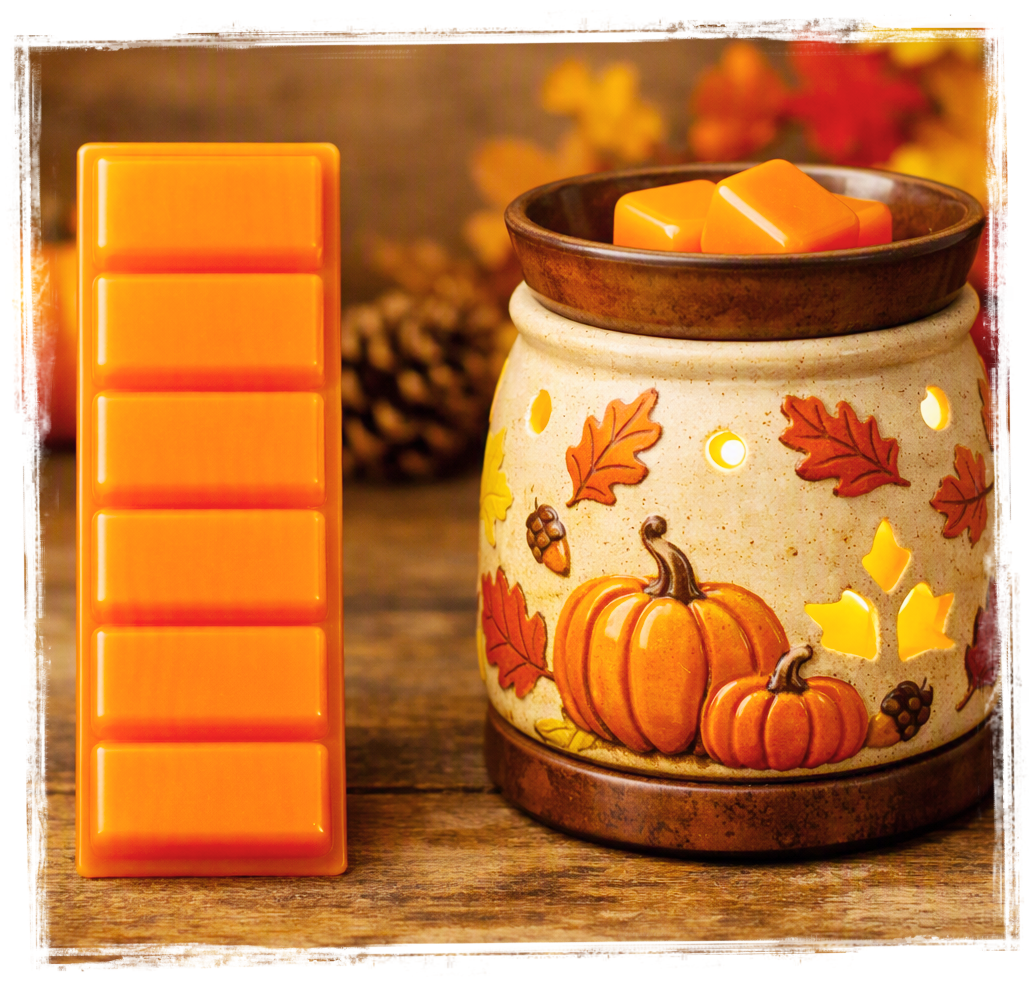 Orange fall wax melts bar beside a lit ceramic wax warmer decorated with autumn leaves and pumpkins on a rustic wood surface