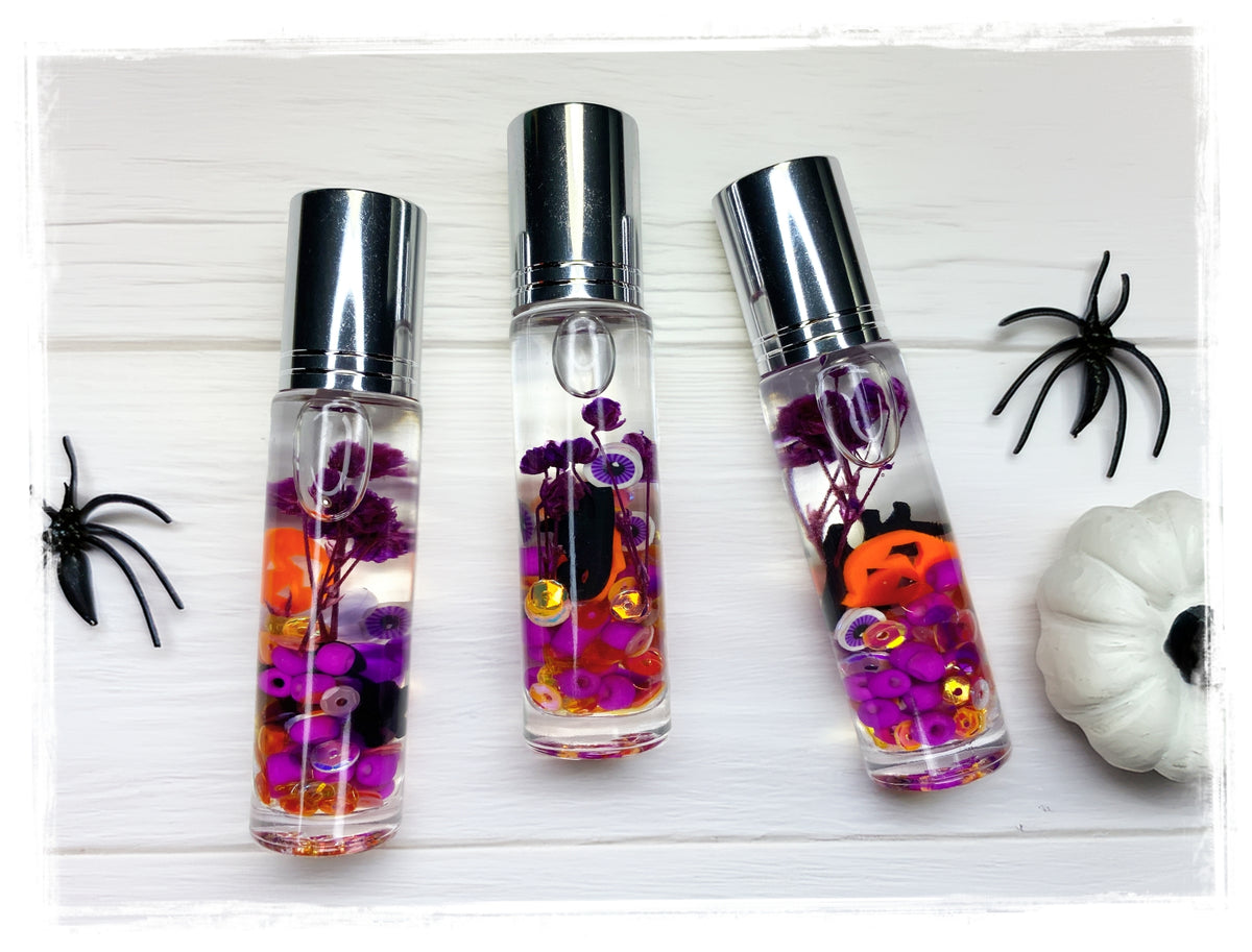 Love Potion Halloween roll-on perfume bottles with orange and purple confetti, styled with black spiders and a white pumpkin.