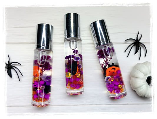 Love Potion Halloween roll-on perfume bottles with orange and purple confetti, styled with black spiders and a white pumpkin.