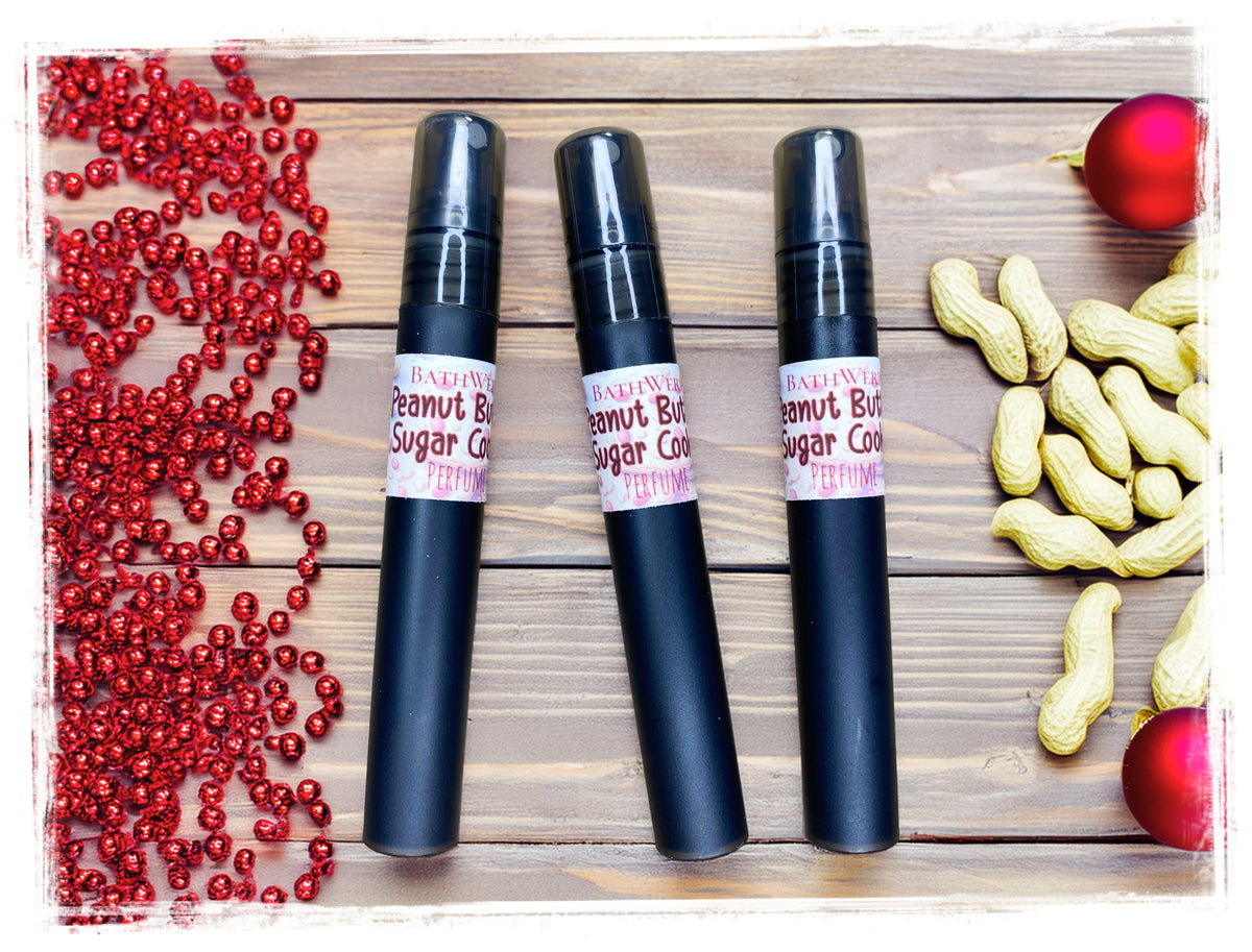 Three BathWerx Peanut Butter Sugar Cookie perfume sprays on a wood background with peanuts, red beads, and ornaments.