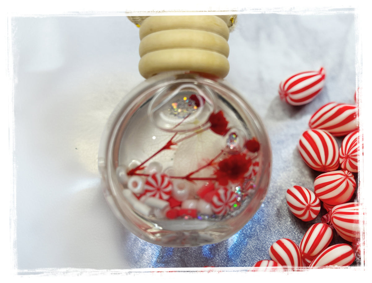 Candy Cane hanging car air freshener in a clear glass bottle with red-and-white peppermint decorations, styled beside striped candies.