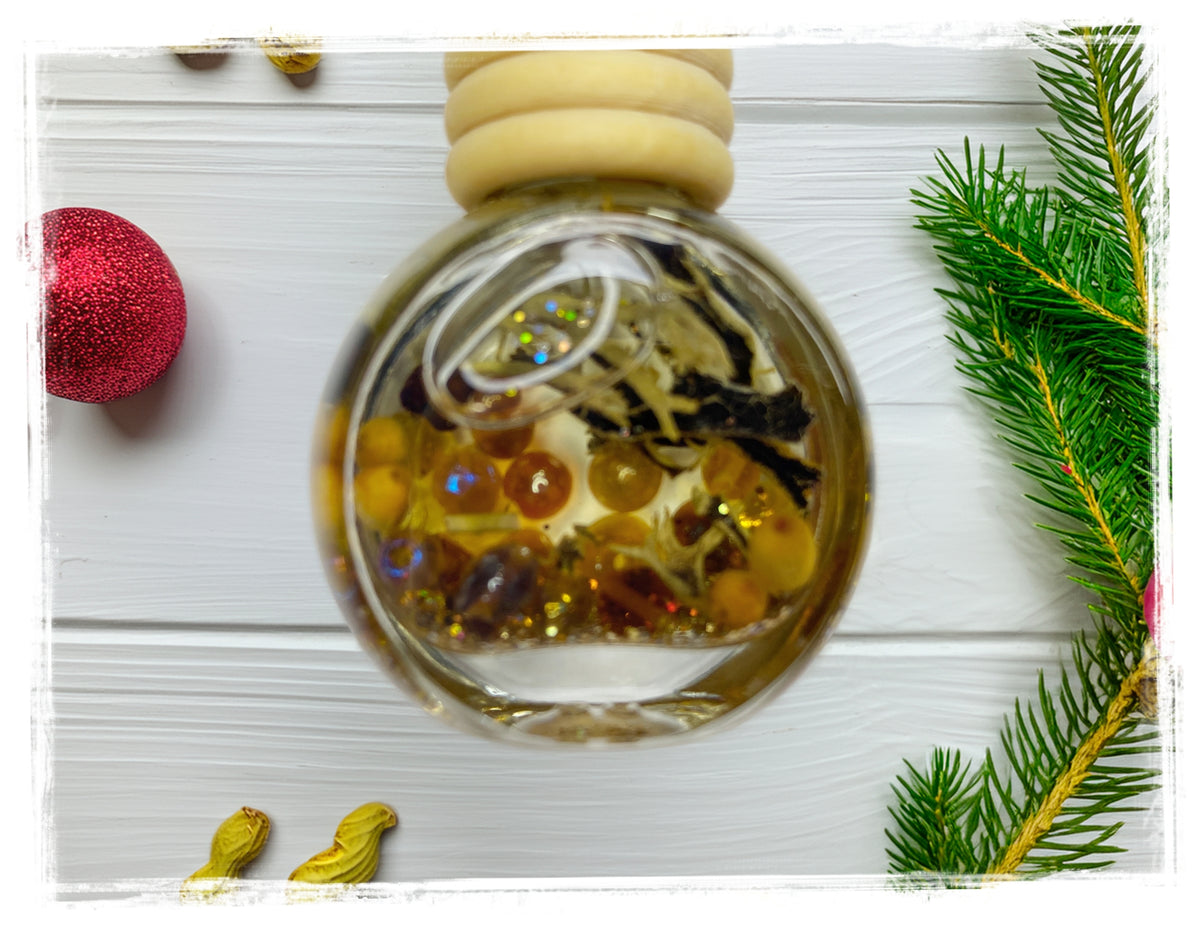 Peanut Butter Sugar Cookie car charm in a round glass bottle with golden accents, styled with pine branches and a red ornament.
