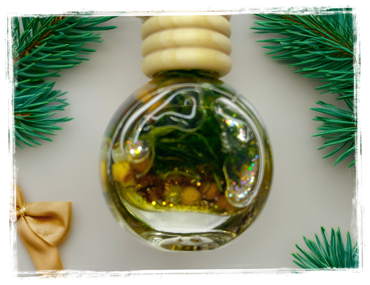 Frasier Fir hanging car air freshener in a round glass bottle with green botanicals and gold accents, framed by fir branches.