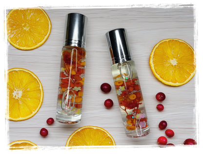 Two Orange Cranberry Spice roll-on perfume oil bottles with silver caps, surrounded by orange slices and cranberries.