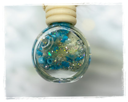 Winter Patchouli car charm with a round glass bottle, wooden cap, blue beads, and shimmering glitter.