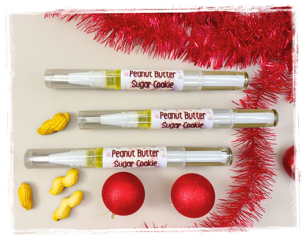 Three Peanut Butter Sugar Cookie nail oil pens with red ornaments, tinsel, and miniature peanut decorations.