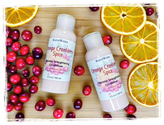 Two bottles of Orange Cranberry Spice intensive strengthening conditioner surrounded by orange slices and cranberries.