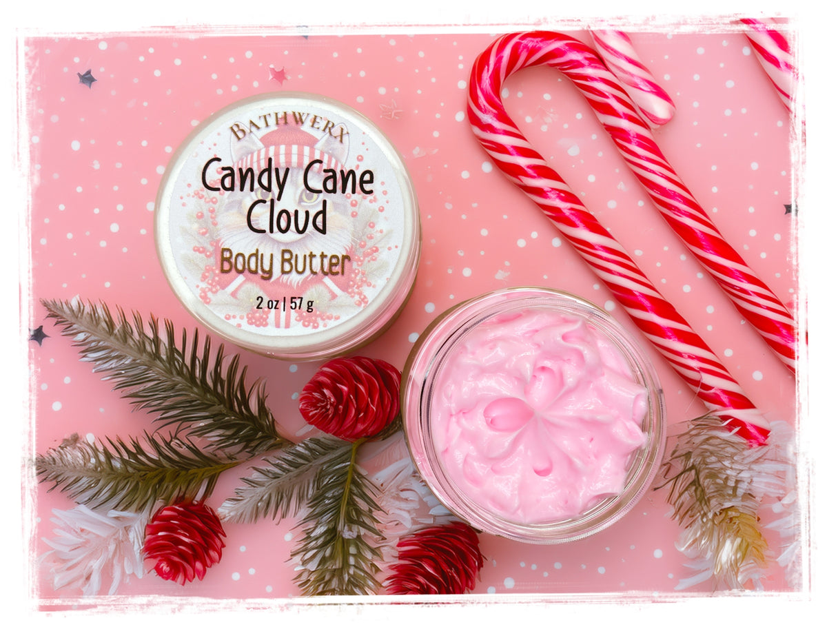 Open jar of pink Candy Cane Cloud Body Butter beside its lid, candy canes, and festive greenery on a pink background.