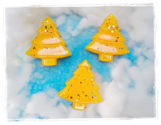 Three golden-orange Christmas tree-shaped soaps in Orange Cranberry Spice, with sparkling accents on a snowy blue-and-white background.