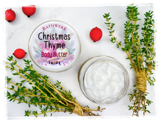 Open jar of Christmas Thyme body butter with white cream, labeled lid, fresh thyme sprigs, and red berries.