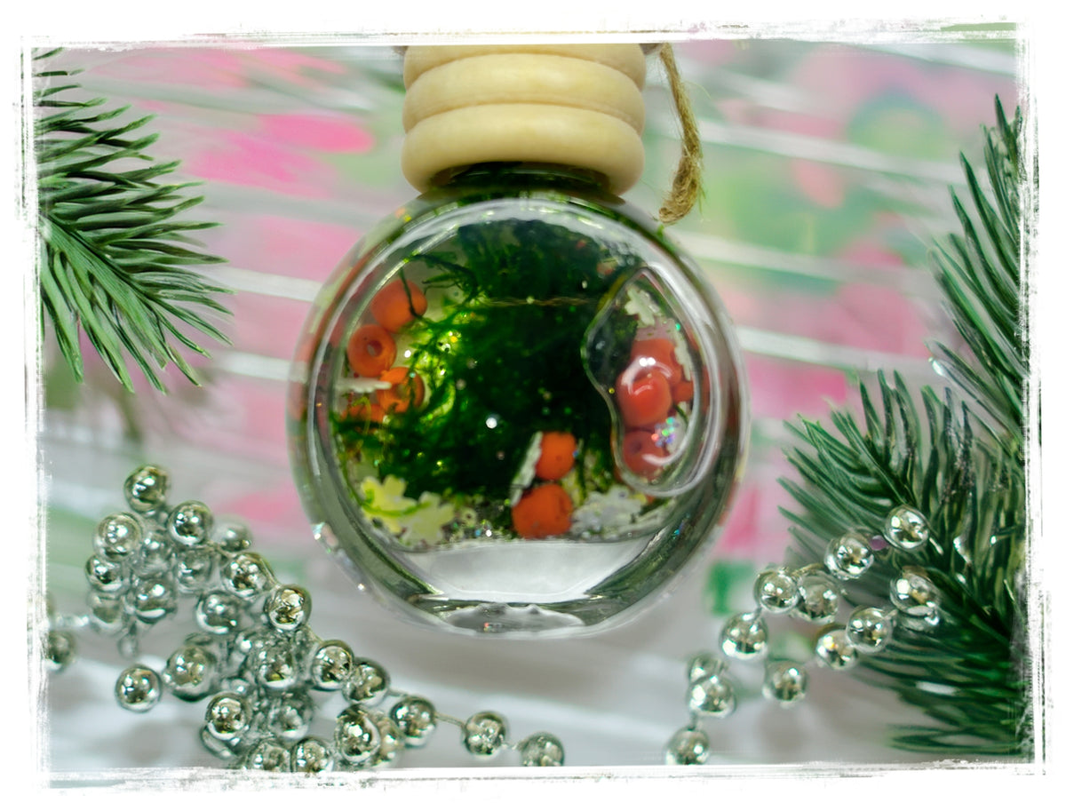 Frasier Fir car charm in a round glass bottle with a wooden cap, surrounded by evergreen branches and silver beads.