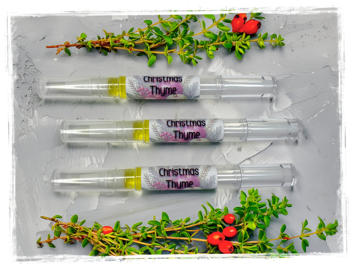 Three Christmas Thyme nail and cuticle oil pens with clear caps, surrounded by thyme sprigs and red berries.