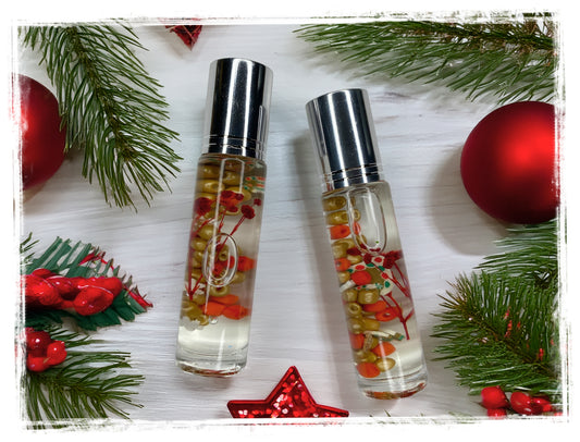 Two Gingerbread Cookie roll-on perfume oil bottles with silver caps and festive accents, surrounded by pine branches and red ornaments.