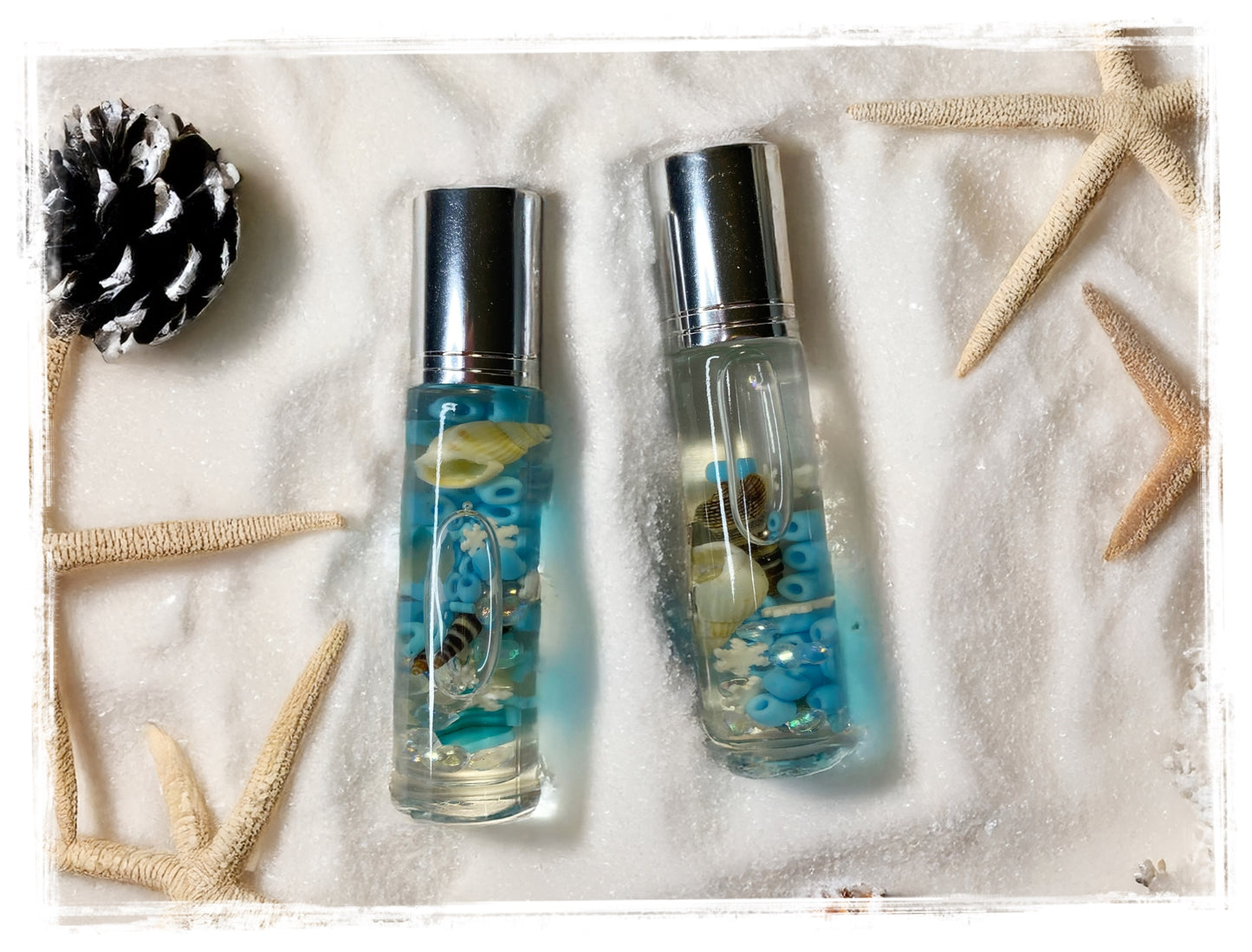 Two small bottles of winter beach perfume and beach-themed decorations on a sandy background.