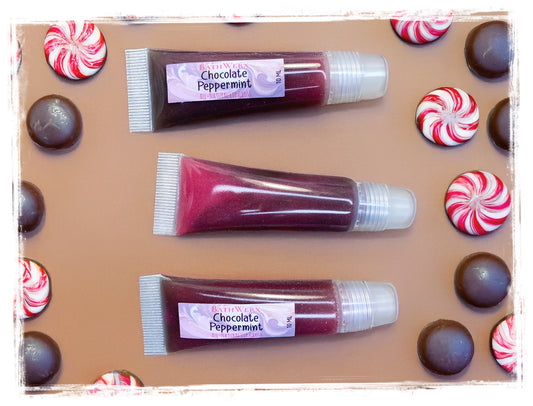 Three tubes of chocolate peppermint lip gloss on a brown surface with candy accents.