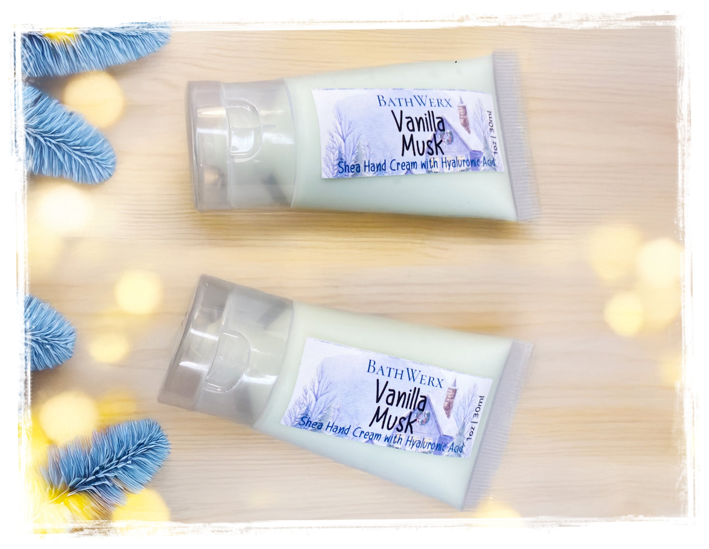 Two tubes of Bath & Body Works Vanilla Musk Shea Hand Cream on a wooden surface with decorative lights and blue flowers.