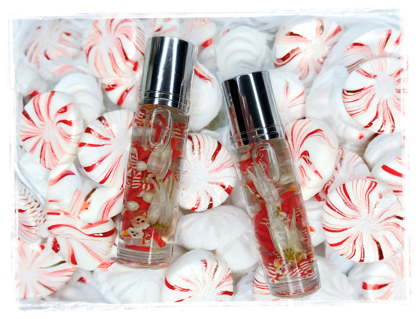 Two small bottles of peppermint milkshake perfume with silver caps surrounded by candy canes and mints on a white background