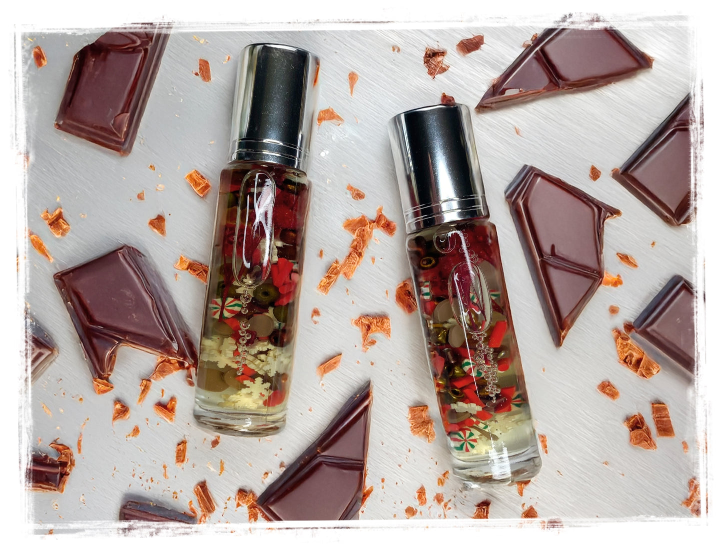 Two small glass bottles with silver caps on a surface with chocolate pieces and orange zest.