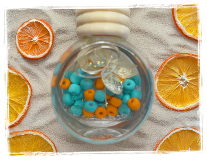 Orange Tide aquatic scented car charm with blue and orange glass beads on sandy beach background