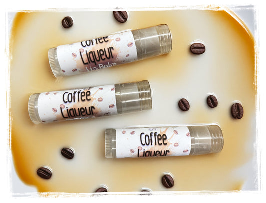 Three lip balms labeled 'Coffee Liqueur' on a surface with coffee beans.