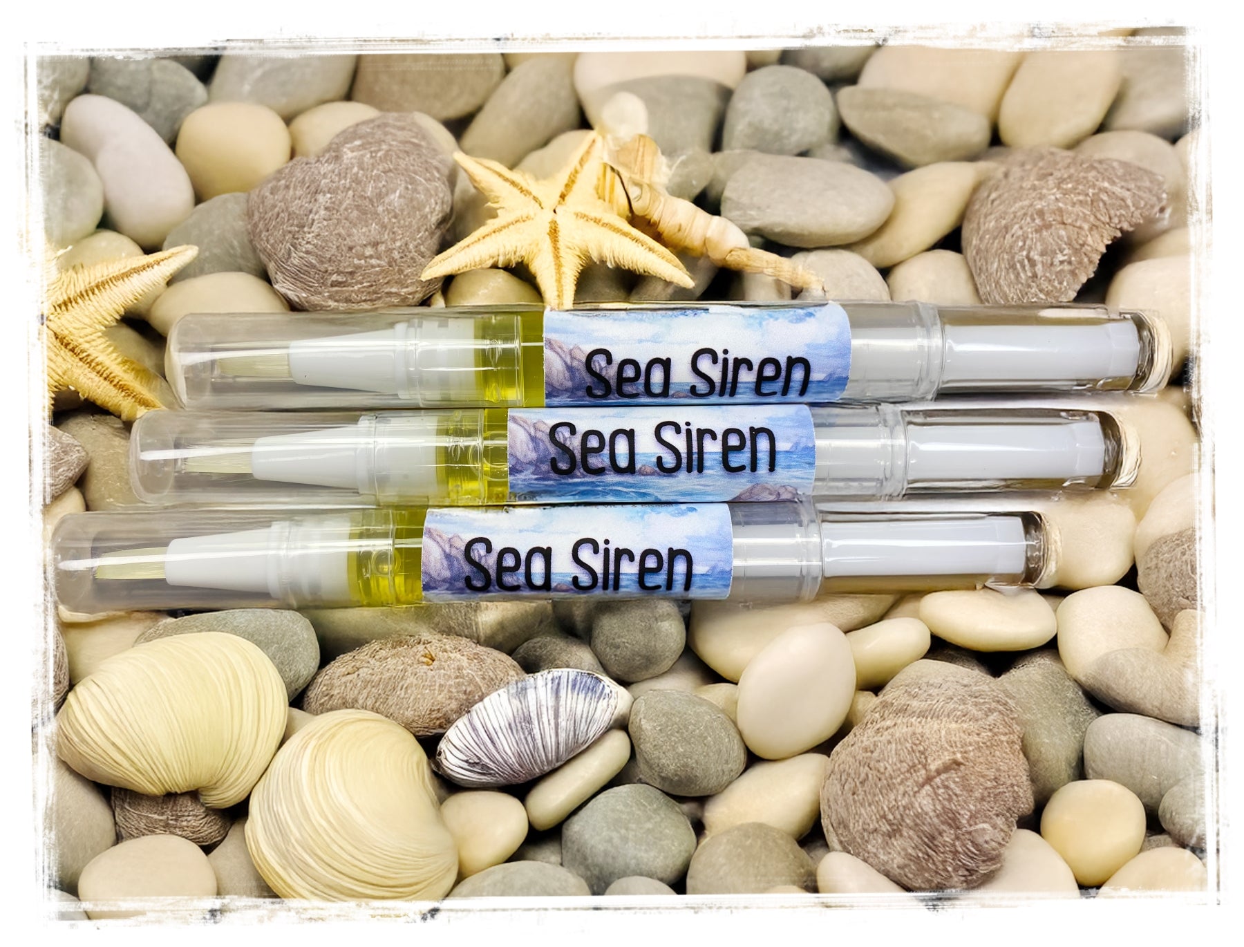 3 Sea Siren Cuticle Nail Pens laying on sea rocks and seashells.