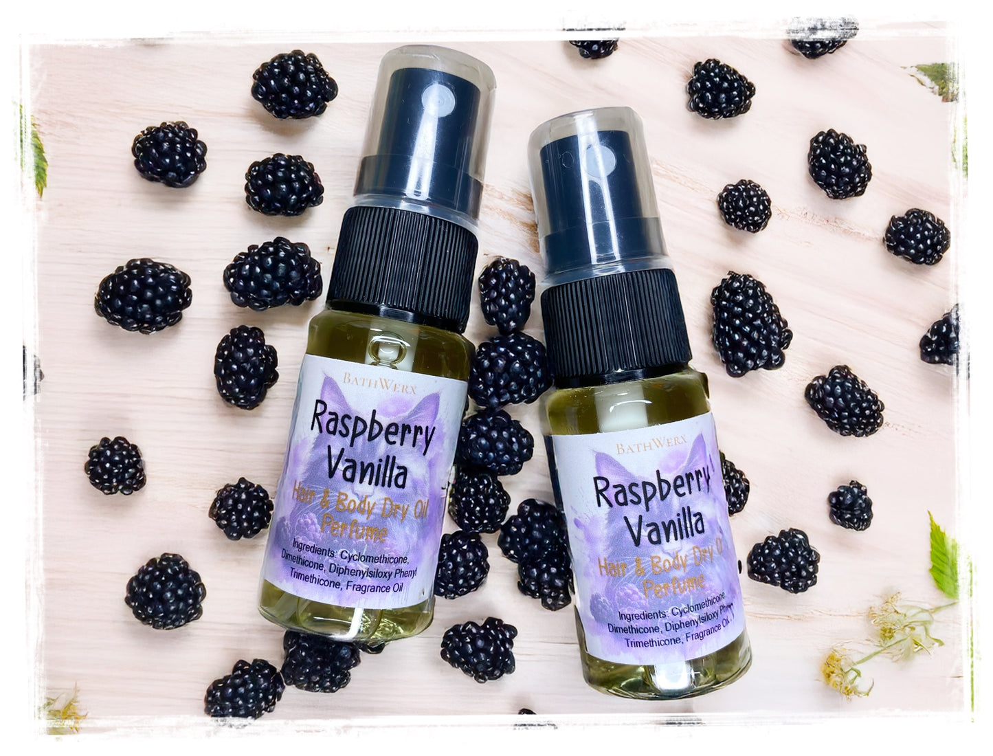 Two bottles of Raspberry Vanilla body oil with blackberries on a light wooden background