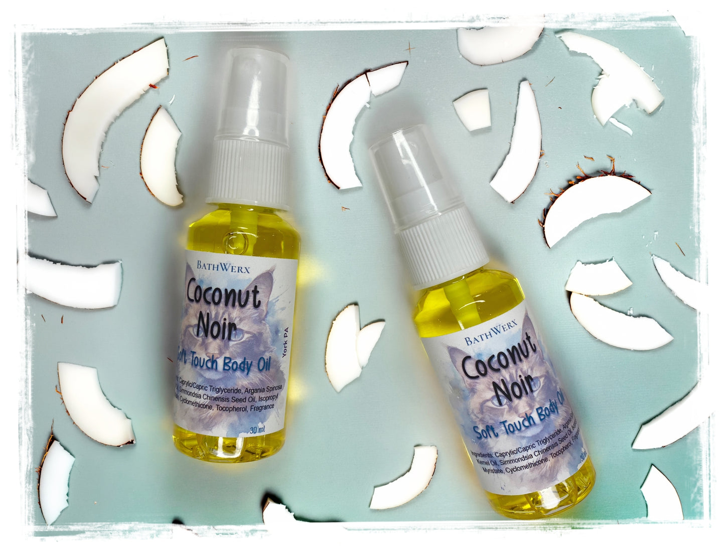 BathWerx Coconut Noir Soft Touch Body Oil – two spray bottles (30ml and travel size) displayed on a light teal surface surrounded by fresh coconut pieces