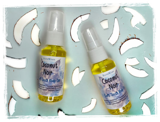 BathWerx Coconut Noir Soft Touch Body Oil – two spray bottles (30ml and travel size) displayed on a light teal surface surrounded by fresh coconut pieces