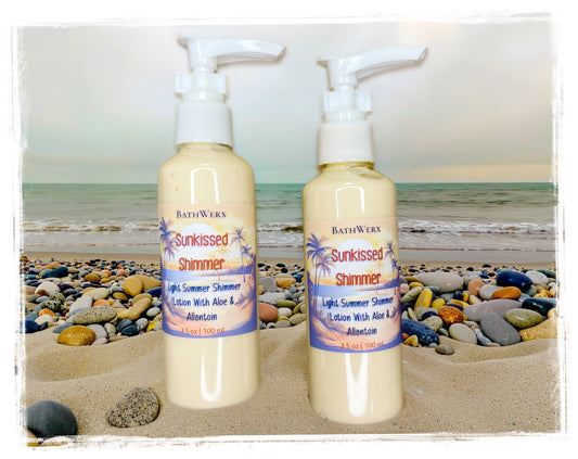 BathWerx Sunkissed Shimmer Lightweight Lotion — two 3.5 oz pump bottles on sandy beach with colorful pebbles and ocean waves in background