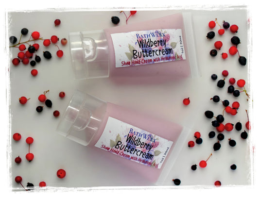 BathWerx Wildberry Buttercream Shea Hand Cream tubes surrounded by scattered red and black wild berries on white surface