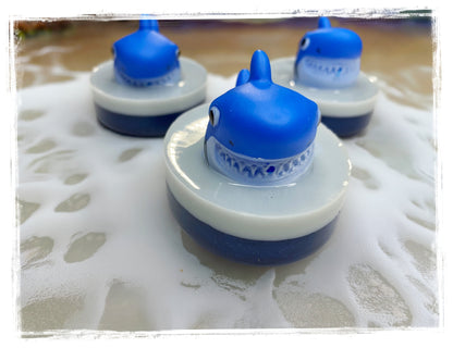 3 BathWerx shark bar soaps scented with blue Hawaiian punch floating in water.